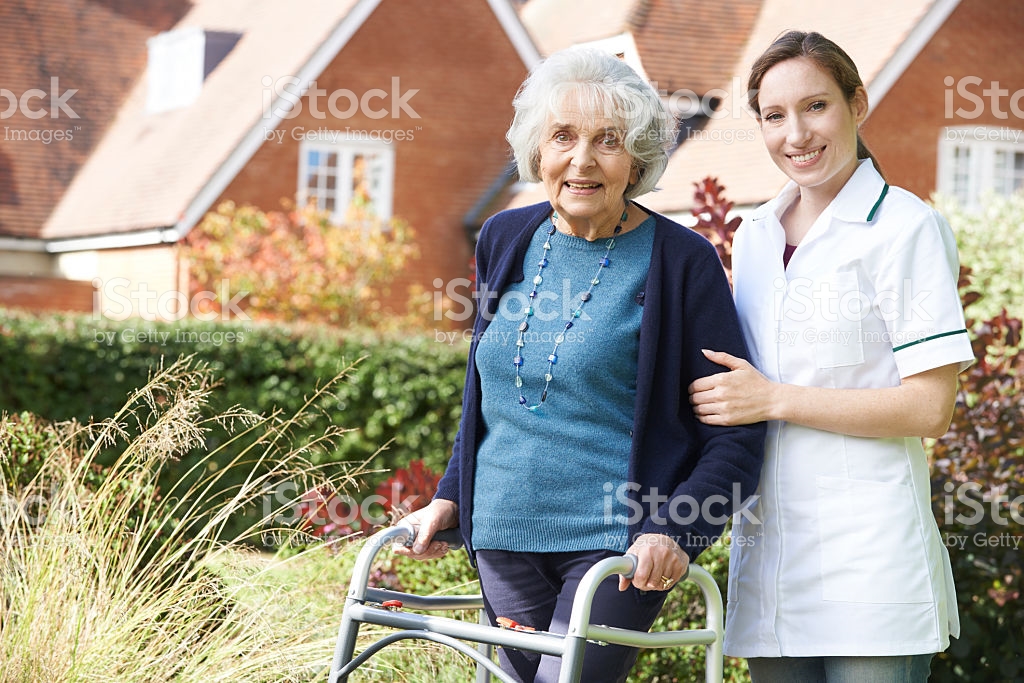 Carer Helping Senior Woman To Walk In Garden Using Walking Frame